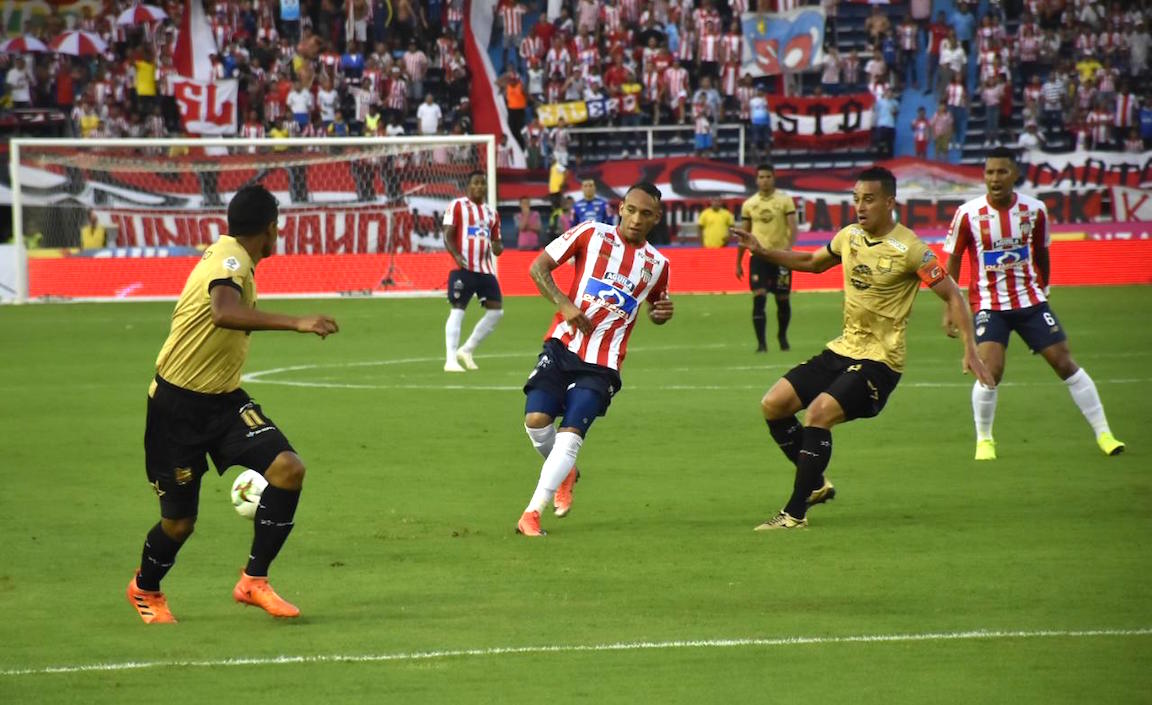 Jarlan Barrera intenando superar a dos rivales.