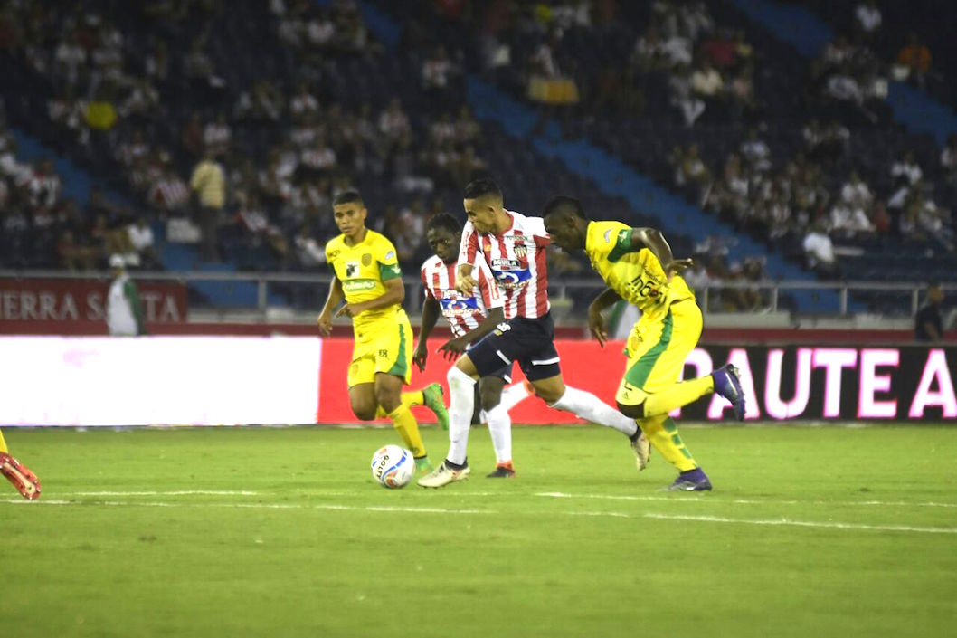 Luis Díaz ensayando un ingreso al arco rival frente a dos visitantes.