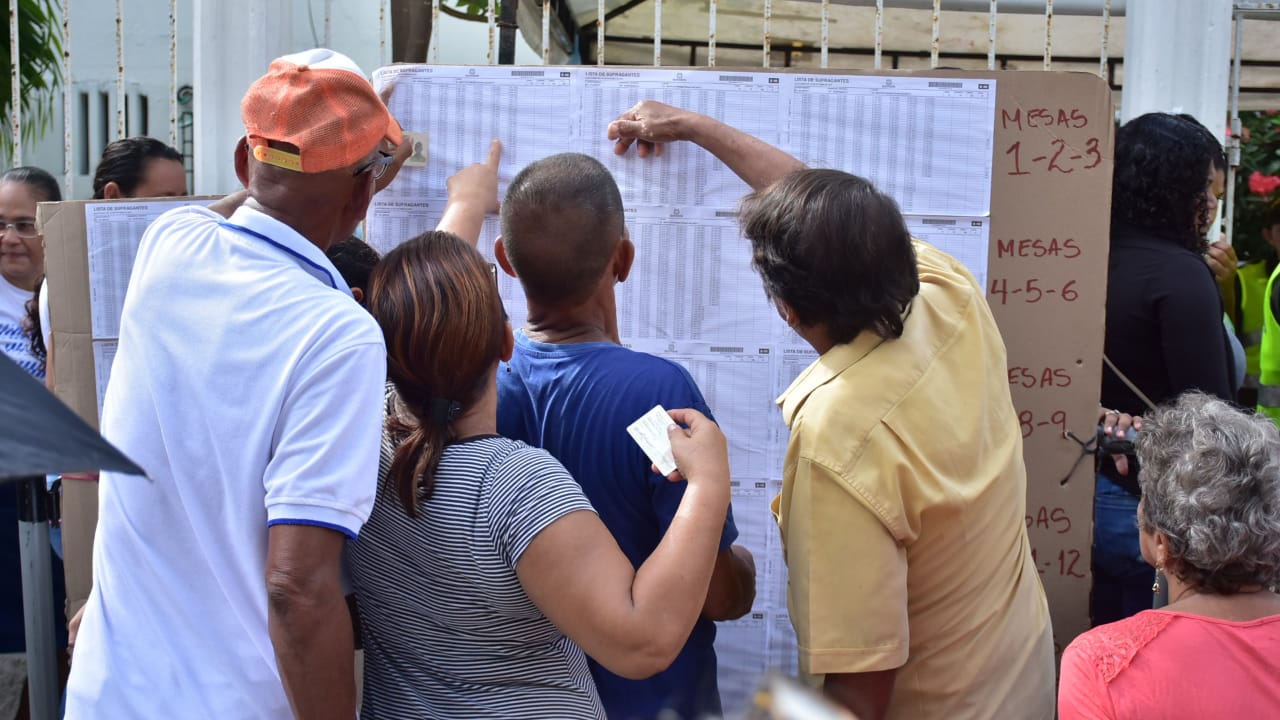 Varias personas consultan en qué mesa ejercerán el derecho al voto.