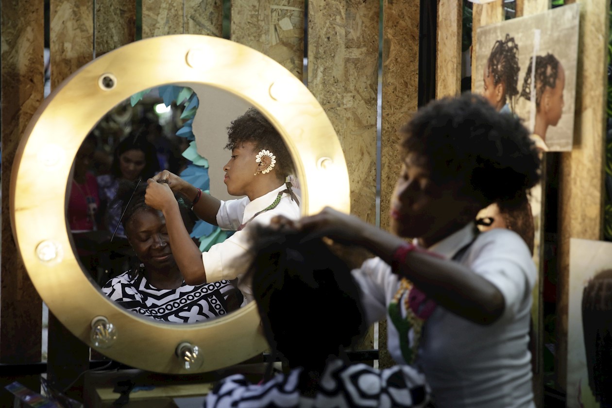 Mujer realiza trenzas a asistente del evento.