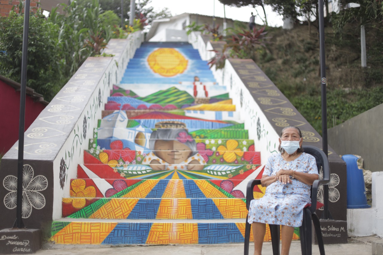 Toñita, sentada frente a la escalera pintada en su honor, en la que se cuentan cinco temas del quehacer usiacureño.