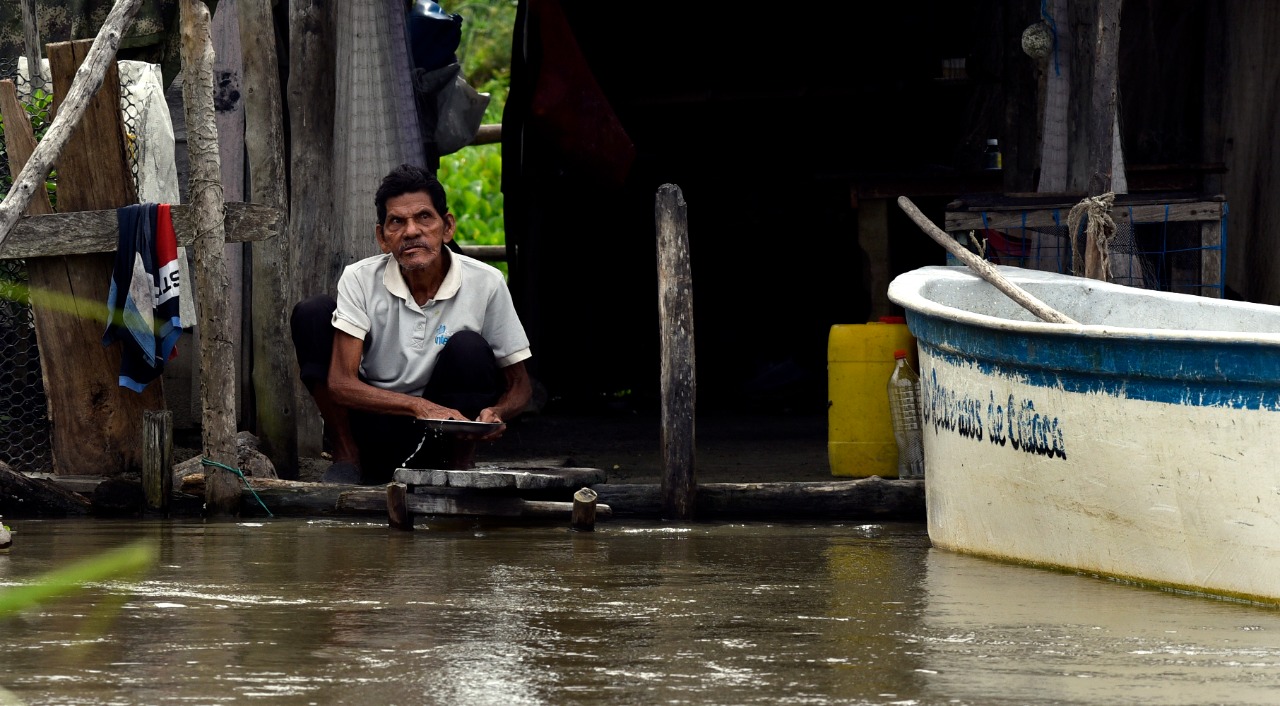 Un adulto mayor lava elementos de cocina en el agua de la Ciénaga Grande