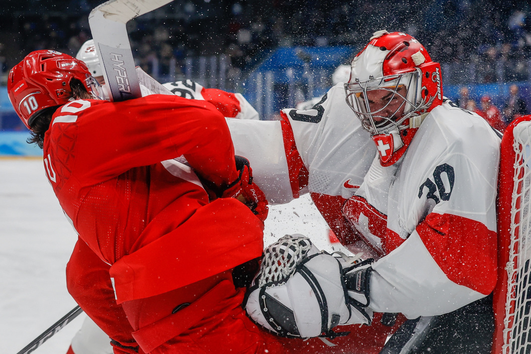 El patinador ruso Dmitri Voronkov (i) choca con el portero suizo Reto Berra durante un partido de la ronda clasificatoria de hockey sobre hielo masculino de los Juegos Olímpicos de Invierno de Pekín 2022 disputado en Pekín (China).