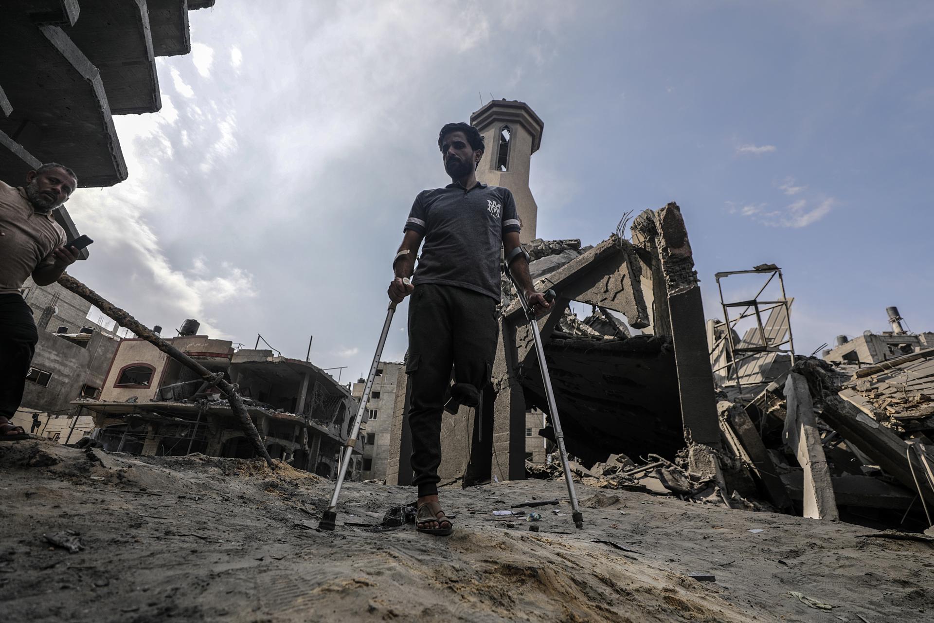 Un hombre palestino camina con muletas mientras inspecciona los daños.