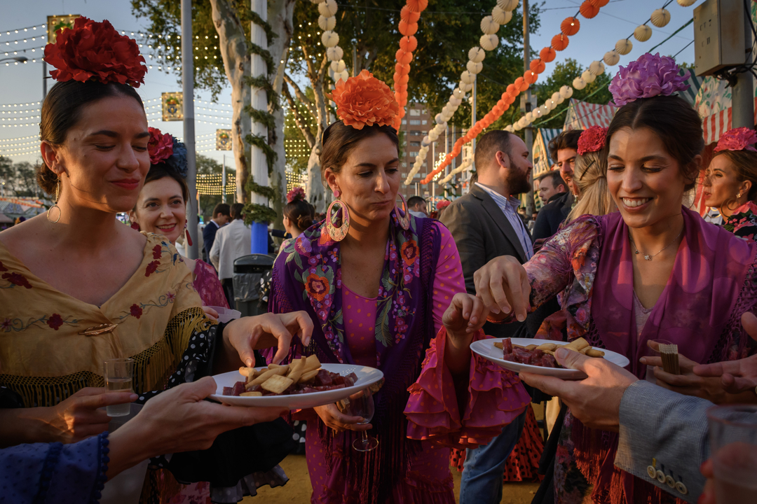 Varias mujeres vestidas de gitana toman chacinas en la feria.