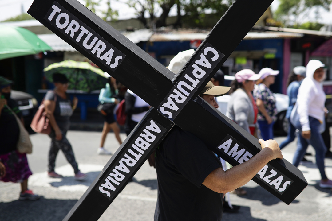 Una persona sostiene una cruz con las palabras escritas "torturas, amenazas, capturas arbitrarias" durante la marcha.