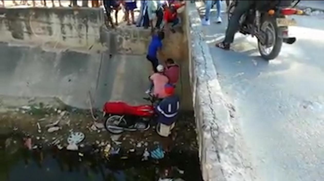 Momento en que vecinos ayudan a subir la moto donde se movilizaban padre e hijo.
