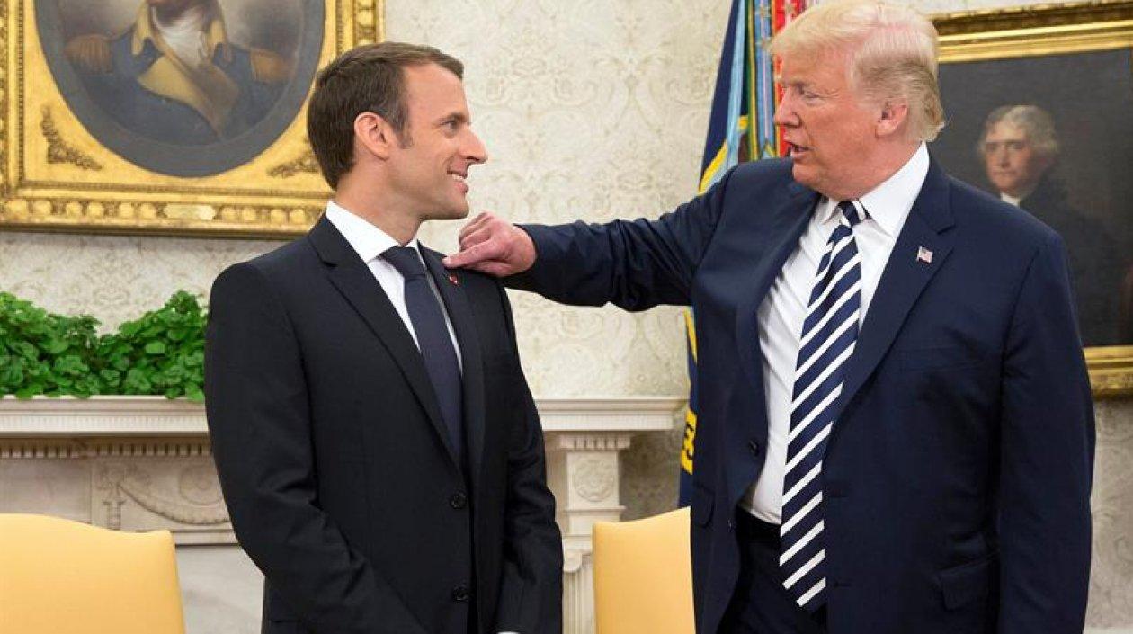 Donald Trump (derecha) le quita algo del hombro al presidente francés Emmanuel Macron.