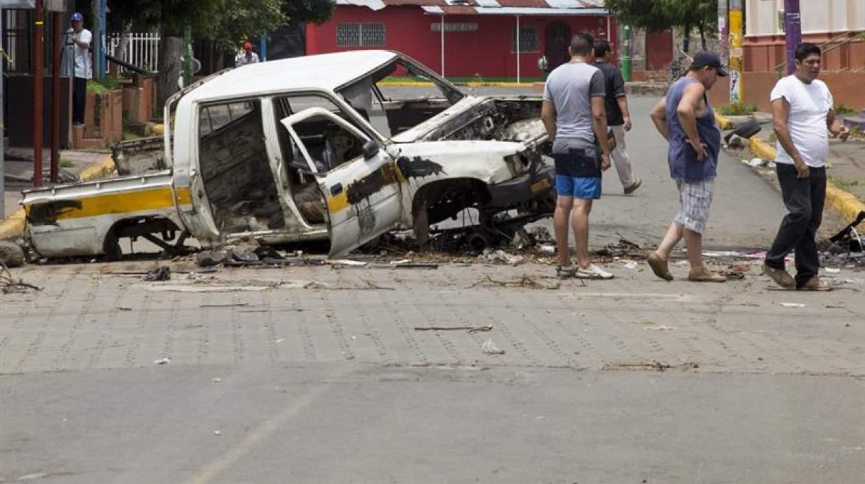 Ciudadanos pasan frente a un coche quemado, en la ciudad de Masaya