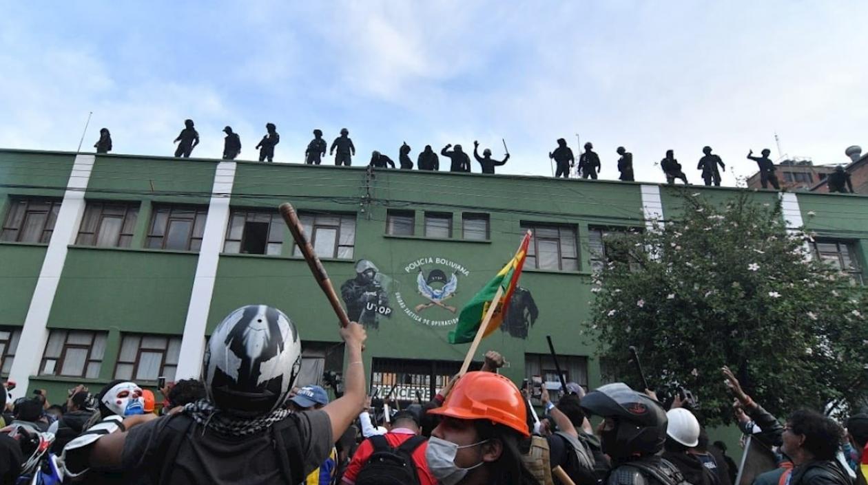 Policías bolivianos saludan desde el techo de una unidad policial a ciudadanos apostados en las puertas de la misma.