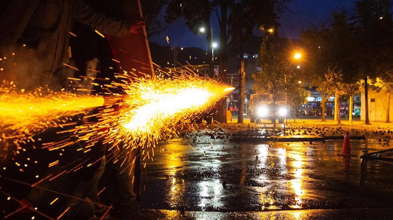Manifestantes lanzan un artefacto contra una tanqueta de la Policía esta noche en Bogotá.