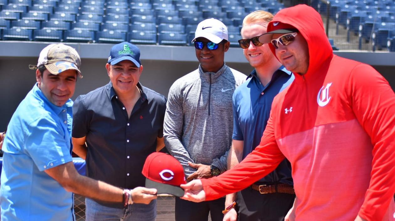 Alejandro Char recibe una gorra de la organización de los Rojos de parte de Trey Hendricks.