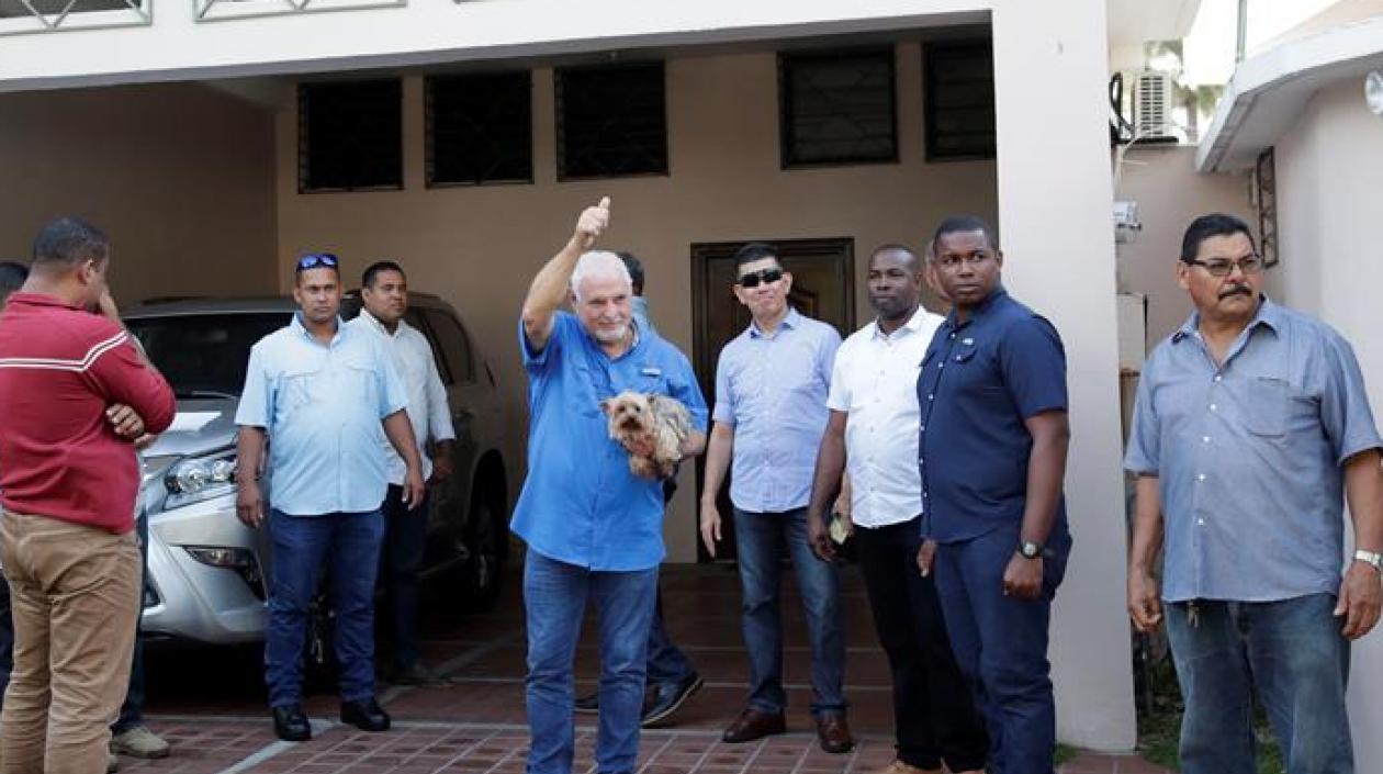 El expresidente de Panamá Ricardo Martinelli (c), rodeado de escoltas privados, saluda mientras sostiene a su perro Martini luego de llegar a su residencia este miércoles.