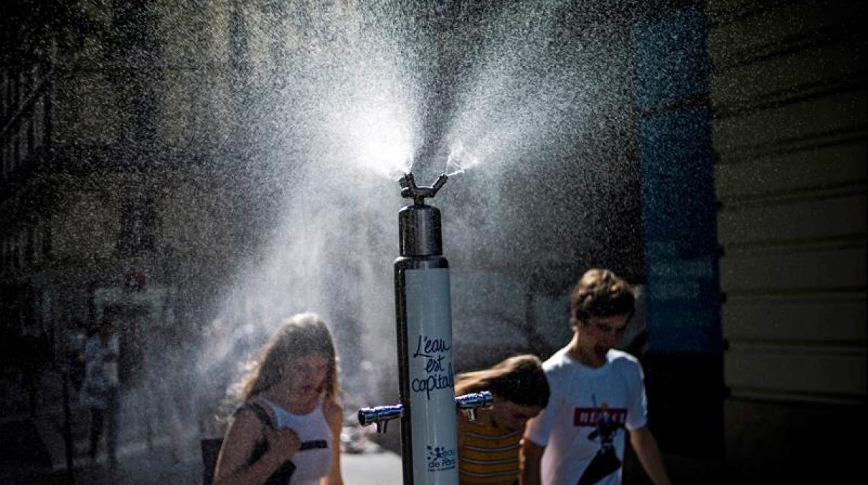  Varios transeúntes se refrescan con pulverizadores de agua públicos debido a las altas temperaturas.