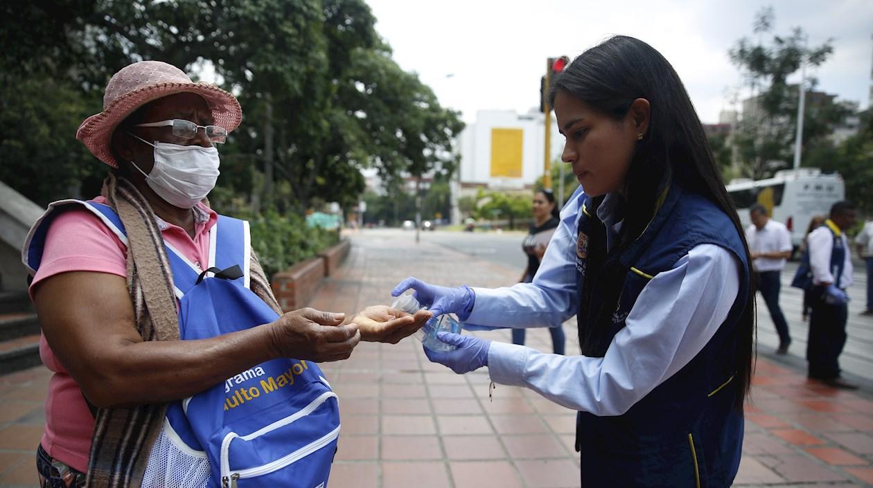 Una joven le suministra gel antibacterial a una adulta mayor en Cali.