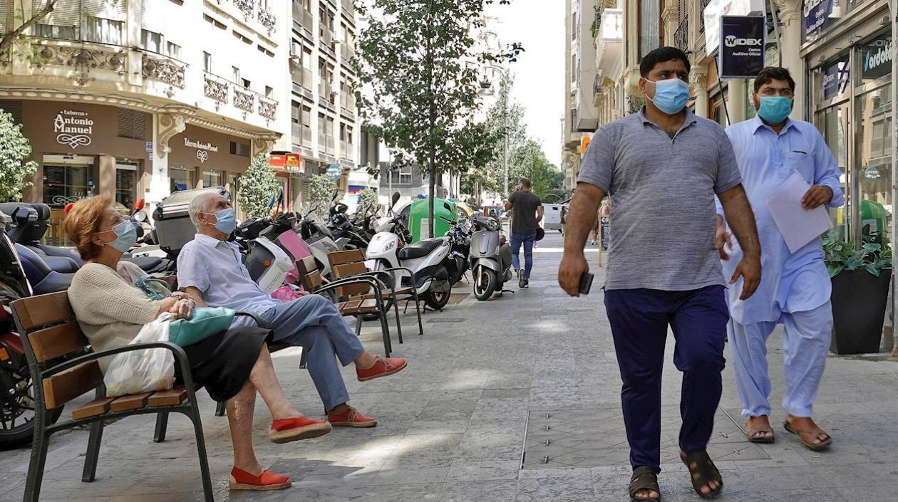 Dos personas descansan sentadas en un banco, mientras otras dos pasan a su lado, todas ellas con tapabocas.