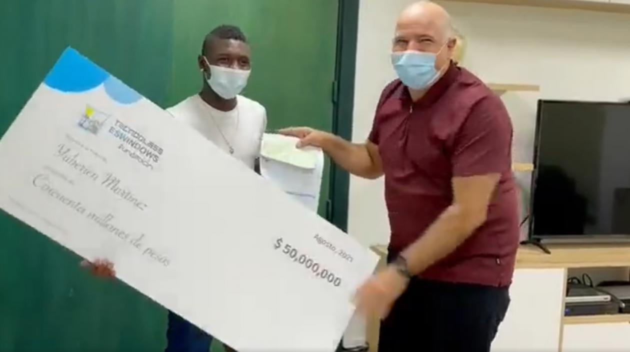 Yuberjen Martínez recibe el cheque de mano de Christian Daes. 