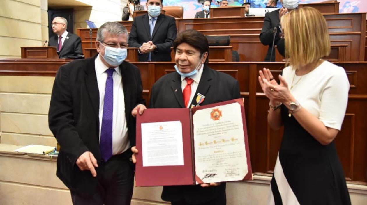 Julio Ernesto Estrada, recibiendo la condecoración por parte de los Representantes Jorge Gómez Vallejo y Jennifer Arias.