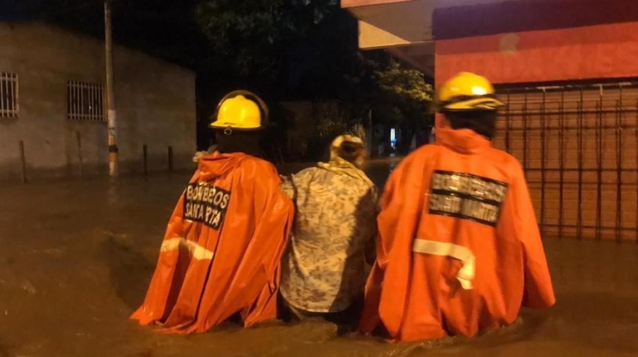 Dos bomberos conducen a una mujer en una calle totalmente inundada de Santa Marta.