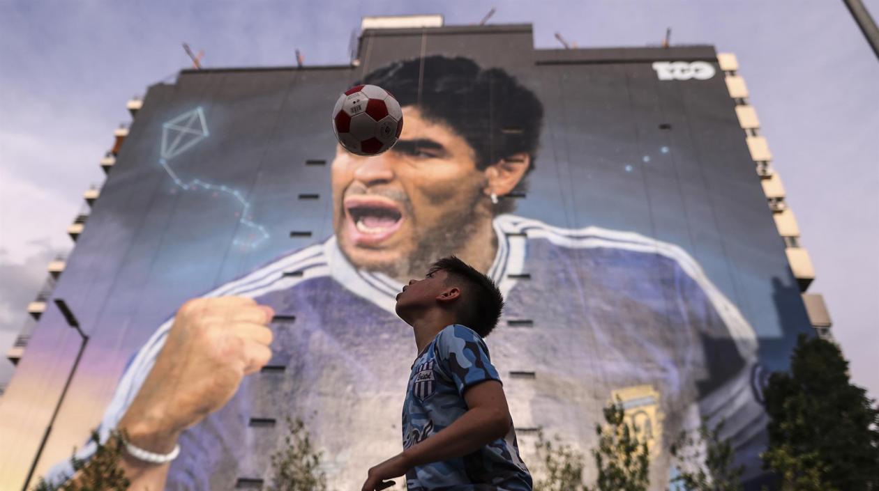 Niño juega con el balón, frente al mural de Diego Maradona. 