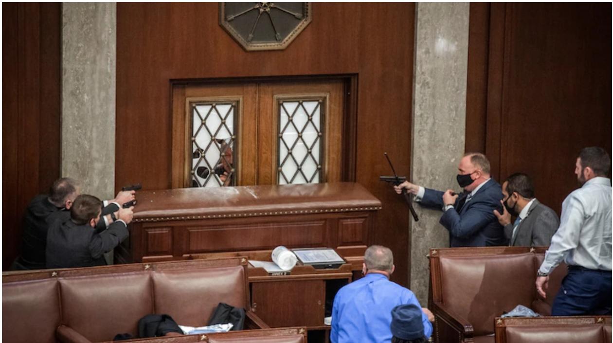 El rostro de un alborotador visto a través de la puerta de vidrio rota de la cámara de la Cámara de Representantes, el 6 de enero de 2021. 