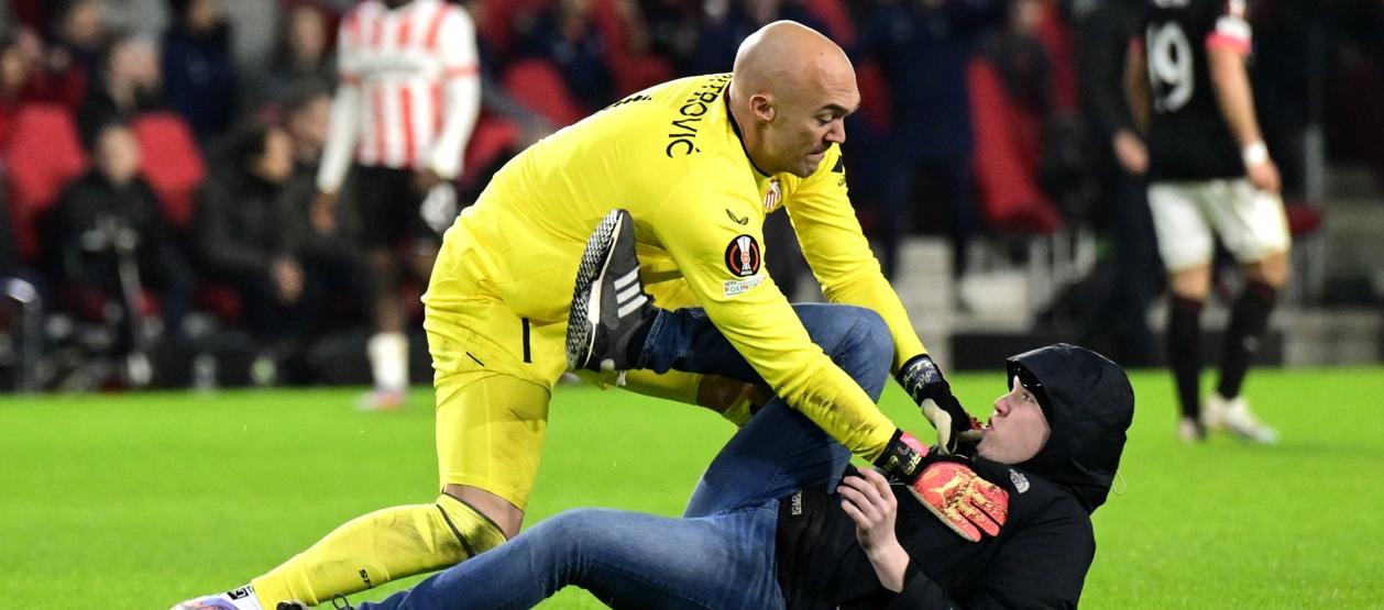 El portero del Sevilla, Marko Dmitrovic, reduce al aficionado que ingresó al campo a agredirlo.