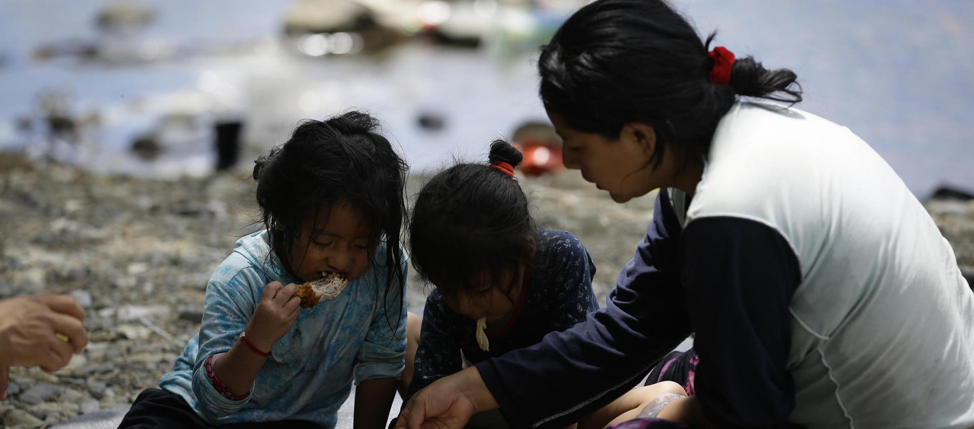Migrante ecuatoriana come junto a sus hijas en el Darién.