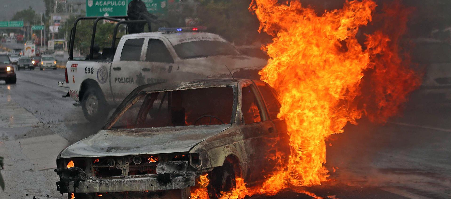 Personal de la policía estatal resguardan la zona donde un vehículo de alquiler fue incendiado.