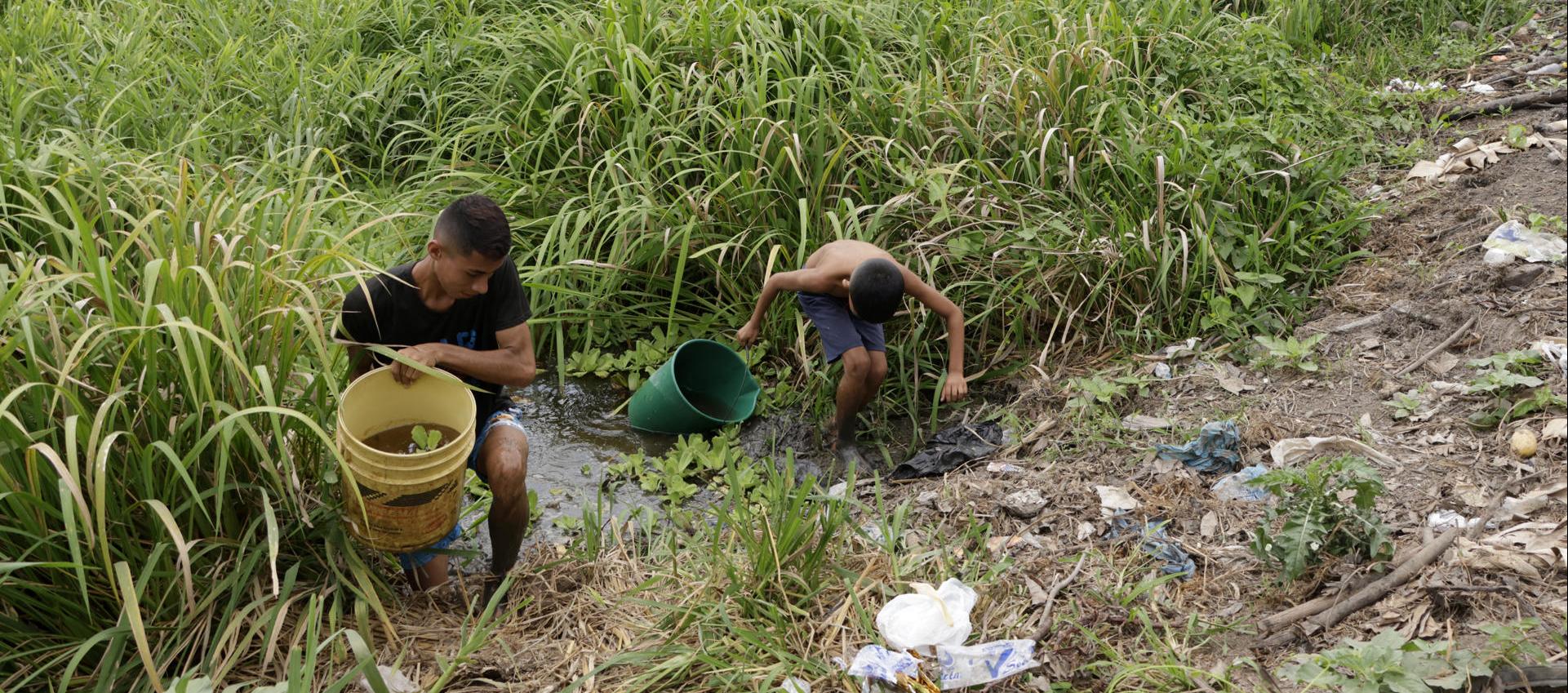 Dos personas sacando agua de un arroyo.