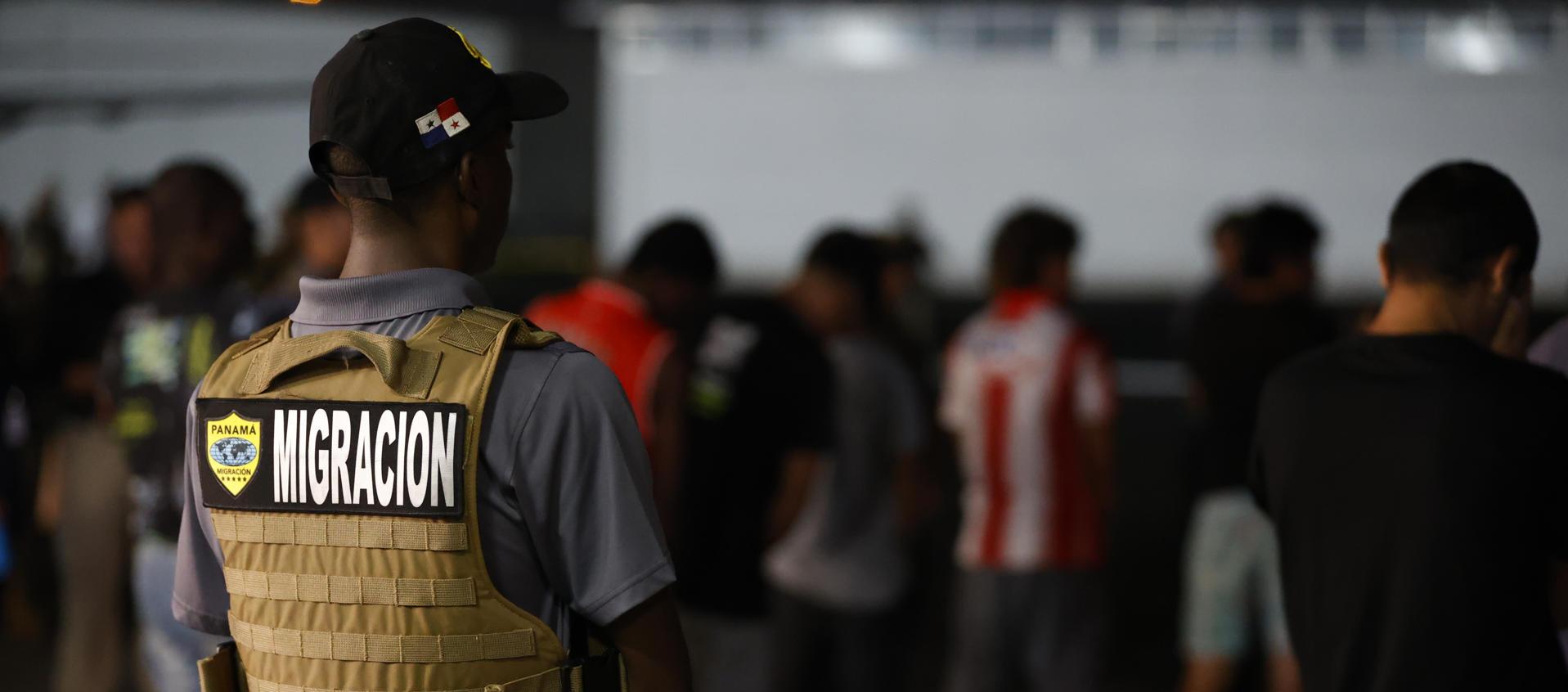 Agente de migración vigila a migrantes antes de ser deportados a Colombia.