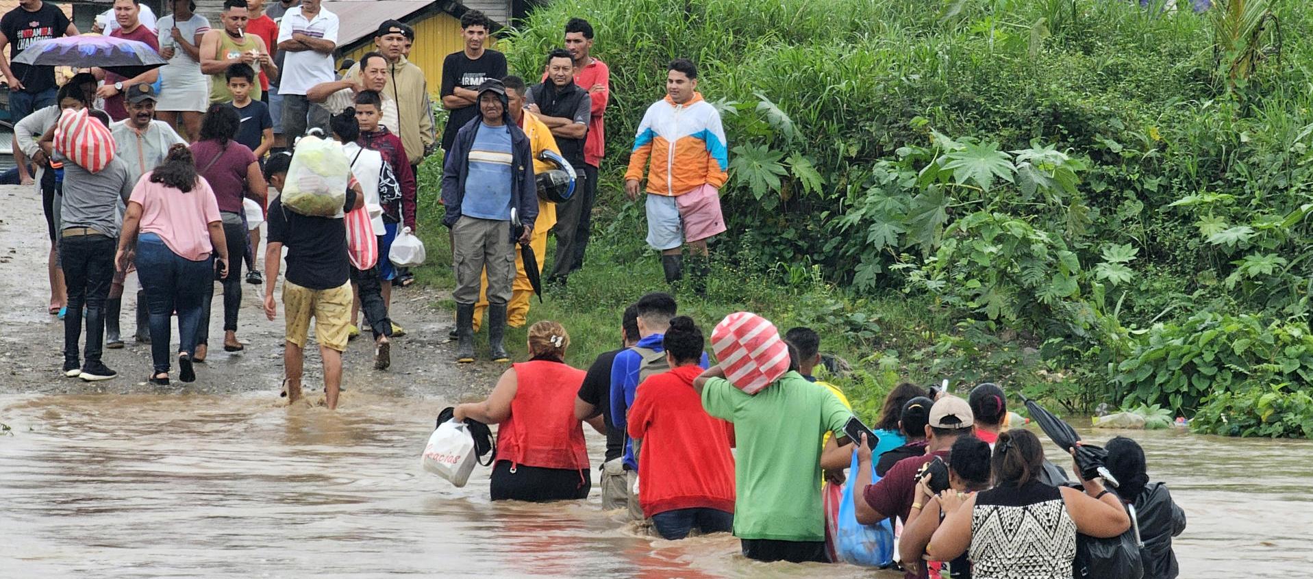 Comunidad cruzando con sus pertenencias por un río en medio de las inundaciones.