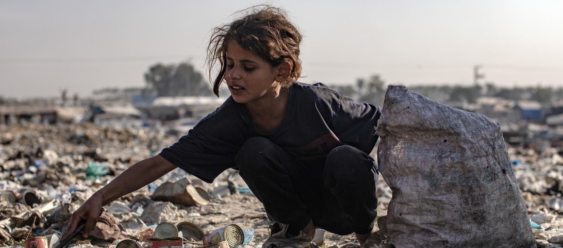 Una niña revisa entre la basura.