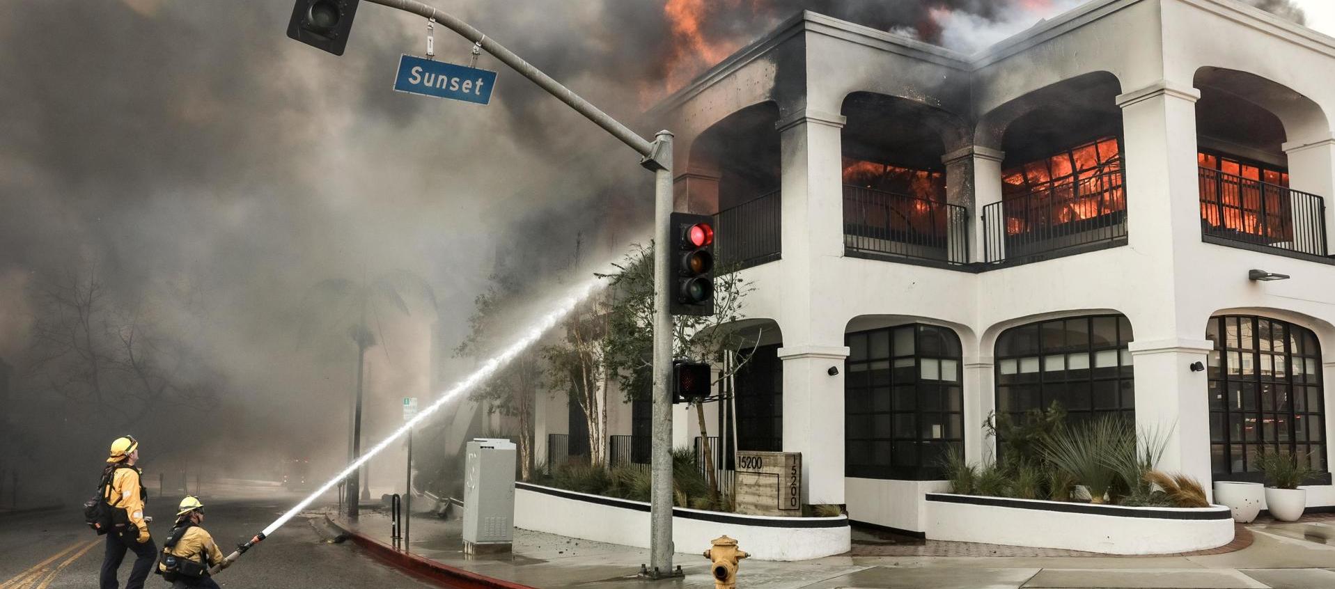 Los bomberos luchan contra las llamas que envuelven un edificio durante el incendio forestal de Palisades. 