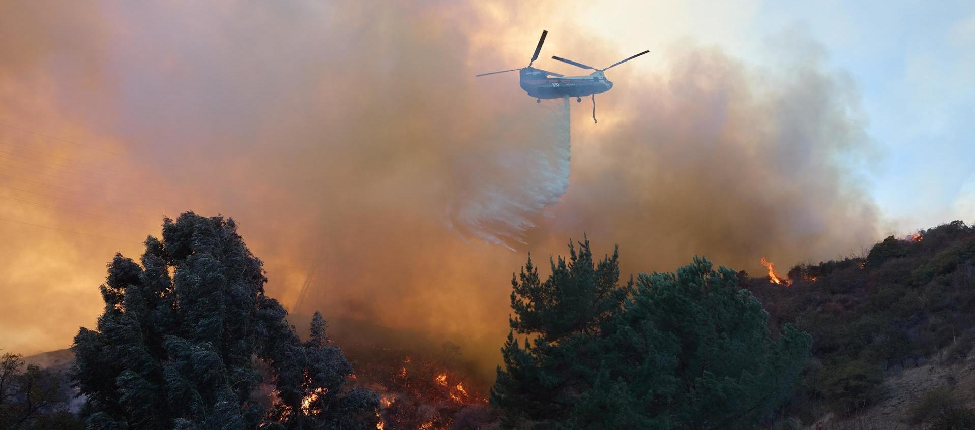Un helicóptero arroja agua sobre una casa durante el incendio forestal en Los Ángeles.