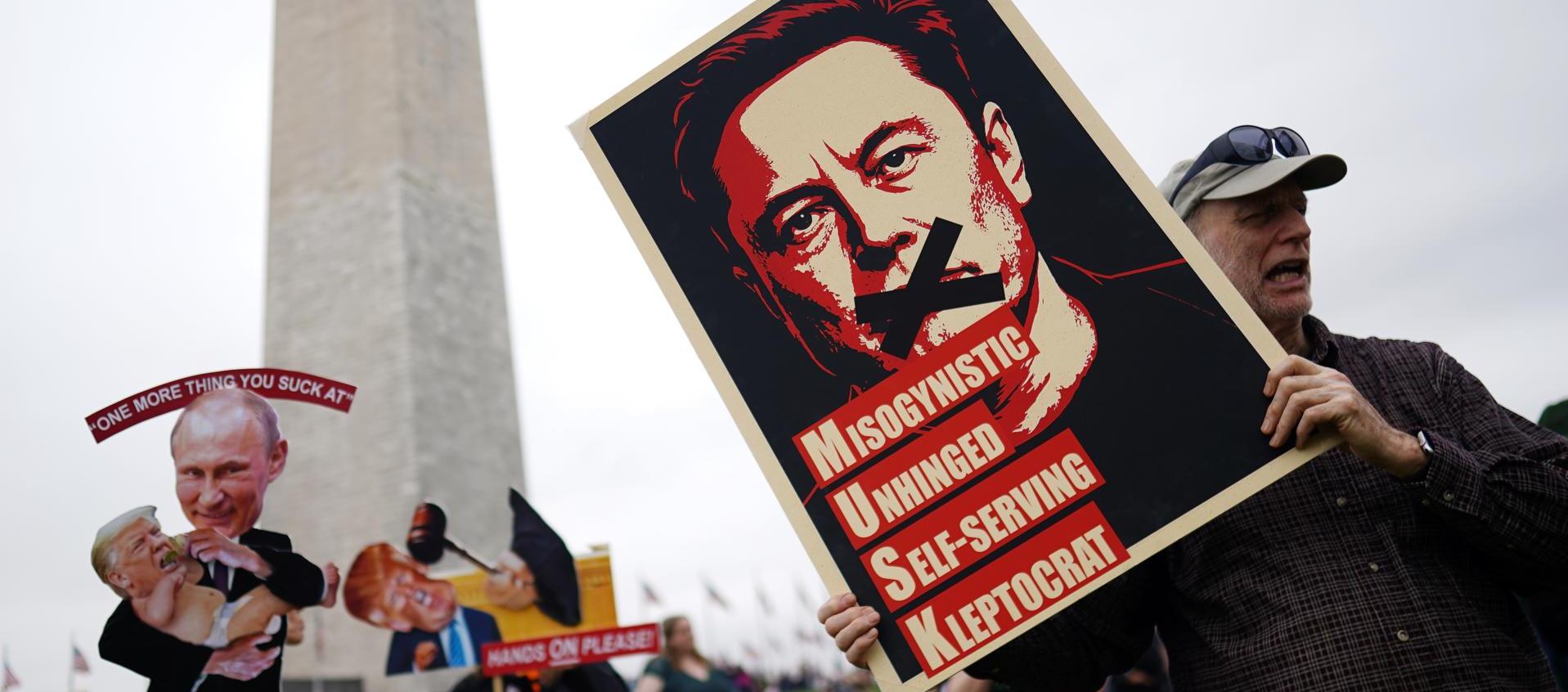 Un manifestante sostiene un cartel que representa a Elon Musk con el texto '¡Manos afuera!' en el National Mall en Washington.
