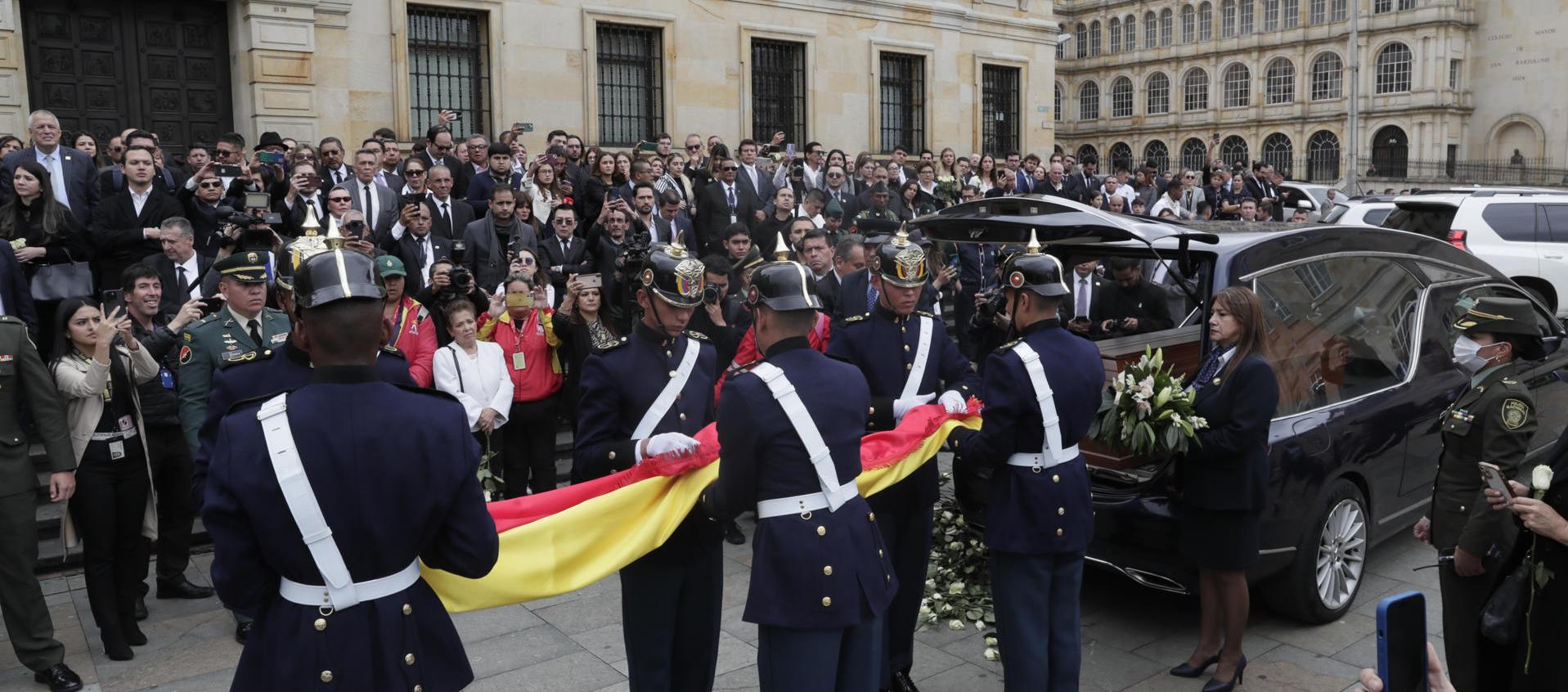 Integrantes del Batallón Guardia Presidencial doblan una bandera de Colombia junto a coche fúnebre con el féretro de Miguel Uribe.