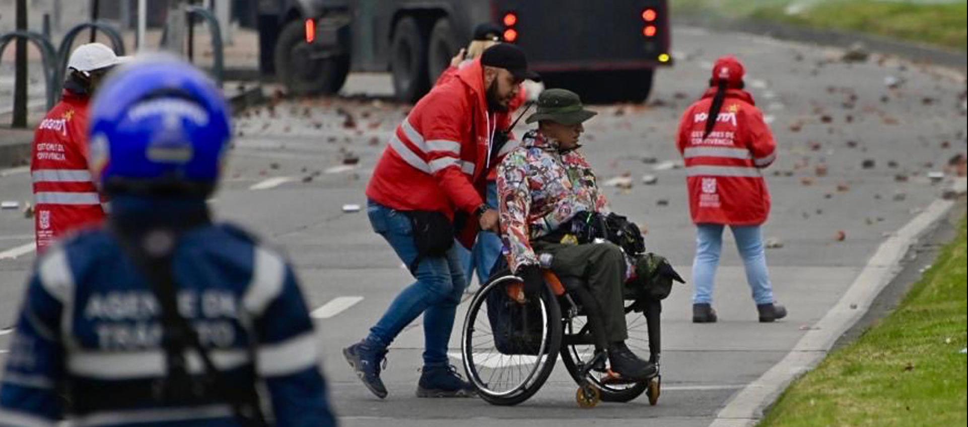 Gestor de convivencia acompañando a una persona en silla de ruedas este viernes, durante protesta en Bogotá.