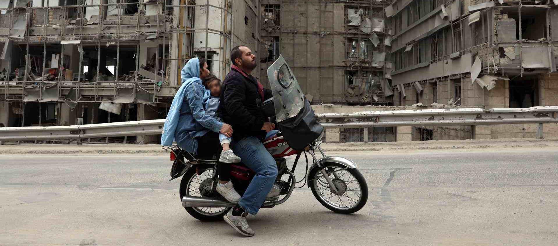 Iraníes pasan en motocicleta frente al hospital Gandhi, destruido en Teherán, Irán.