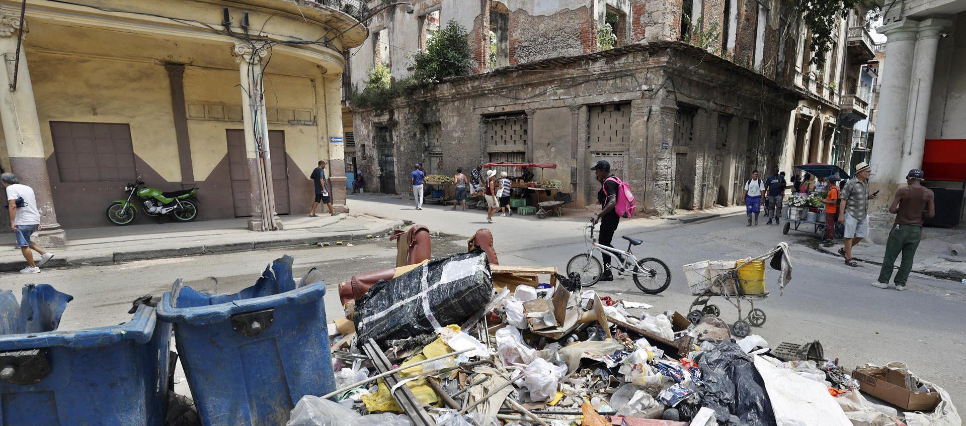 Personas caminan frente a basura acumulada por la falta de combustible para su recolección.