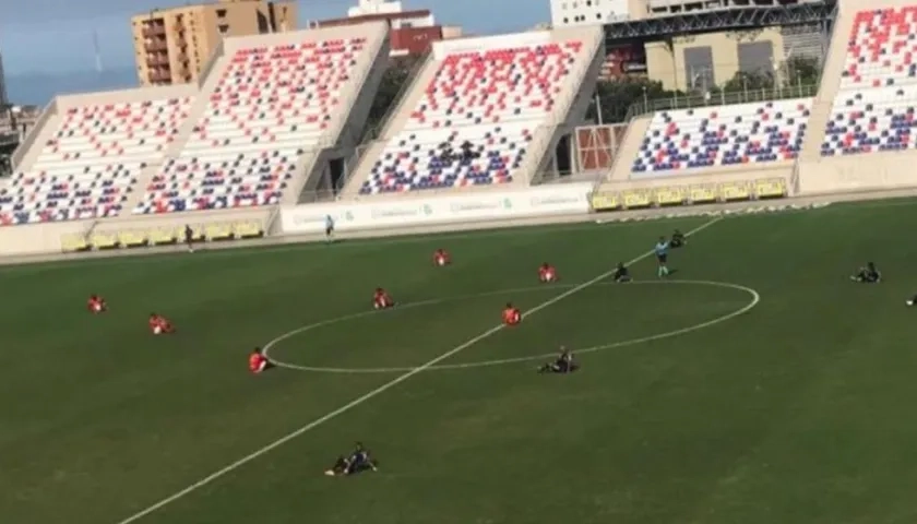 Jugadores del Barranquilla FC y del Deportivo Pereira se sientan en la cancha. 