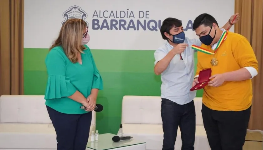Alcalde Pumarejo condecora al estudiante Alejandro Salas por su puntaje perfecto de las Pruebas Saber 11. Observa la secretaria de educación, Bibiana Rincón.