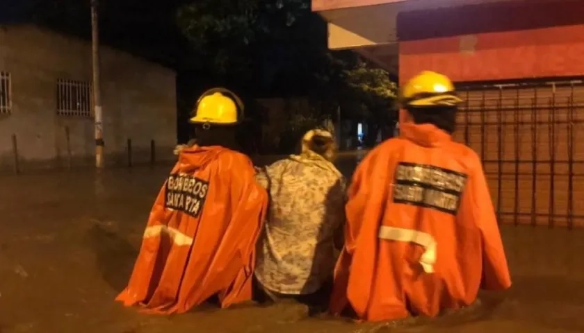 Dos bomberos conducen a una mujer en una calle totalmente inundada de Santa Marta.