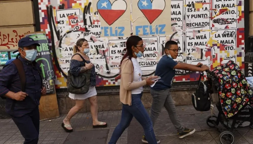 Varias personas caminan frente a una pared con información relacionada al plebiscito constitucional del domingo en Chile.