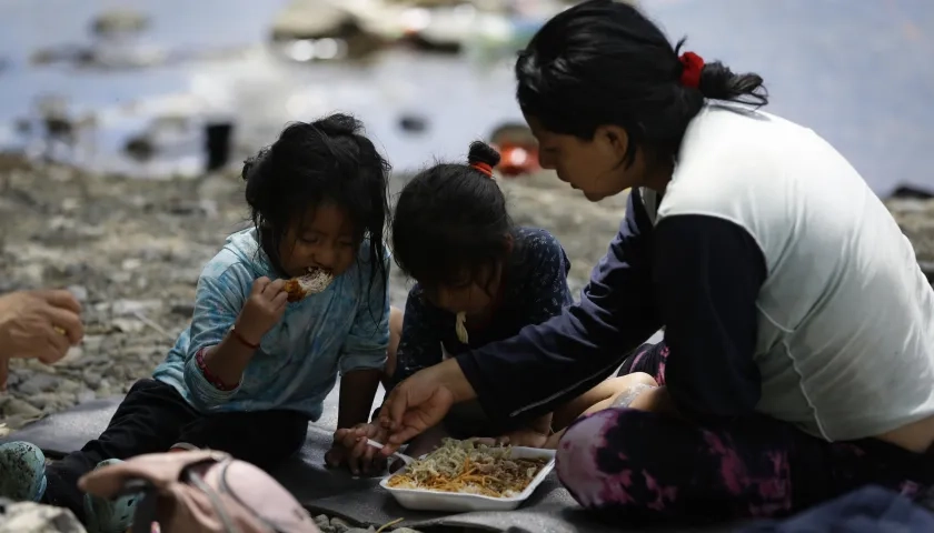 Migrante ecuatoriana come junto a sus hijas en el Darién.