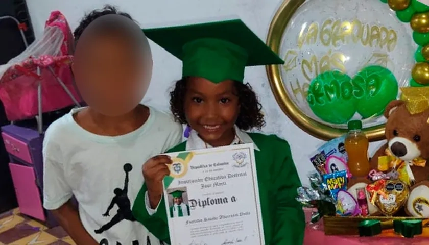La niña con su diploma de grado y al lado de su hermanito