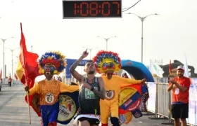 Gerard Giraldo cruza la meta escoltado por dos personajes carnavaleros. 