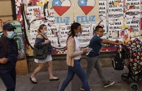 Varias personas caminan frente a una pared con información relacionada al plebiscito constitucional del domingo en Chile.