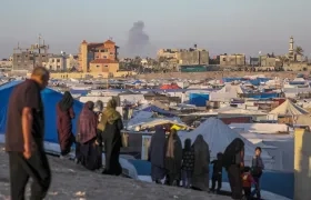 Desplazados internos palestinos y al fondo tras un ataque aéreo israelí en Rafah.