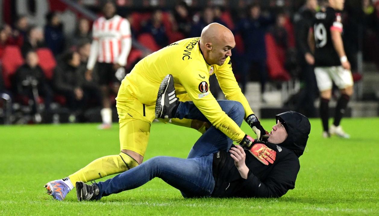 El portero del Sevilla, Marko Dmitrovic, reduce al aficionado que ingresó al campo a agredirlo.