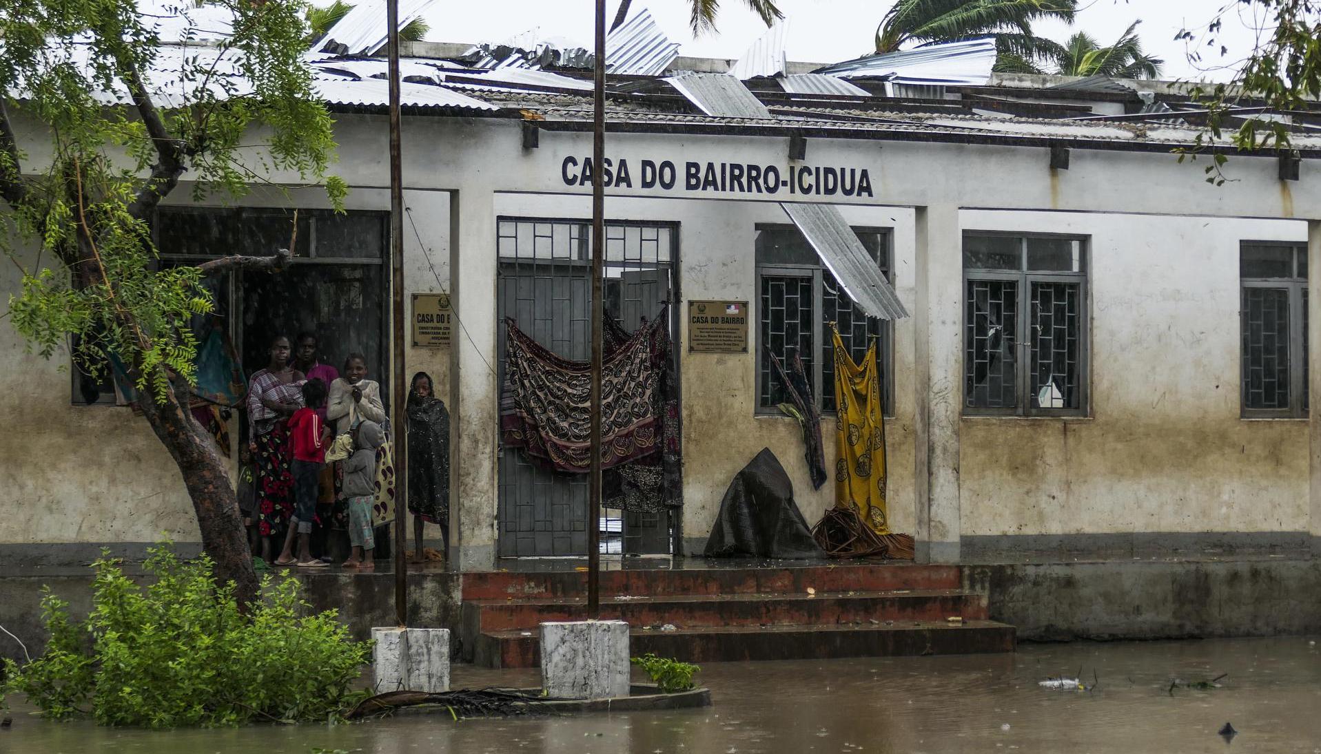 Varias personas se protegen de la lluvia en una calle inundada tras de la destrucción causada por el ciclón Freddy en Quelimane, Mozambique.